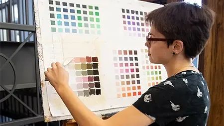 Female student paining a grid of color swatches.